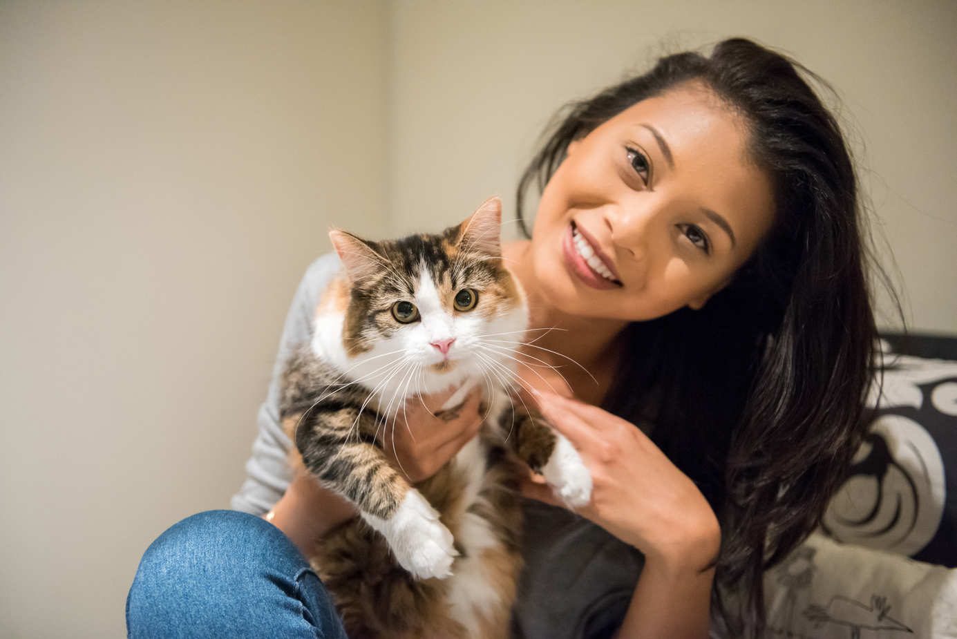 A woman holding her cat up in her lap looking at the camera