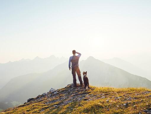 A man with a dog stands on top of a mountain