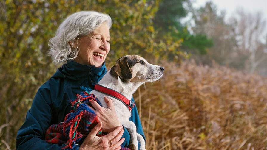 Woman holding dog in a blanket outside