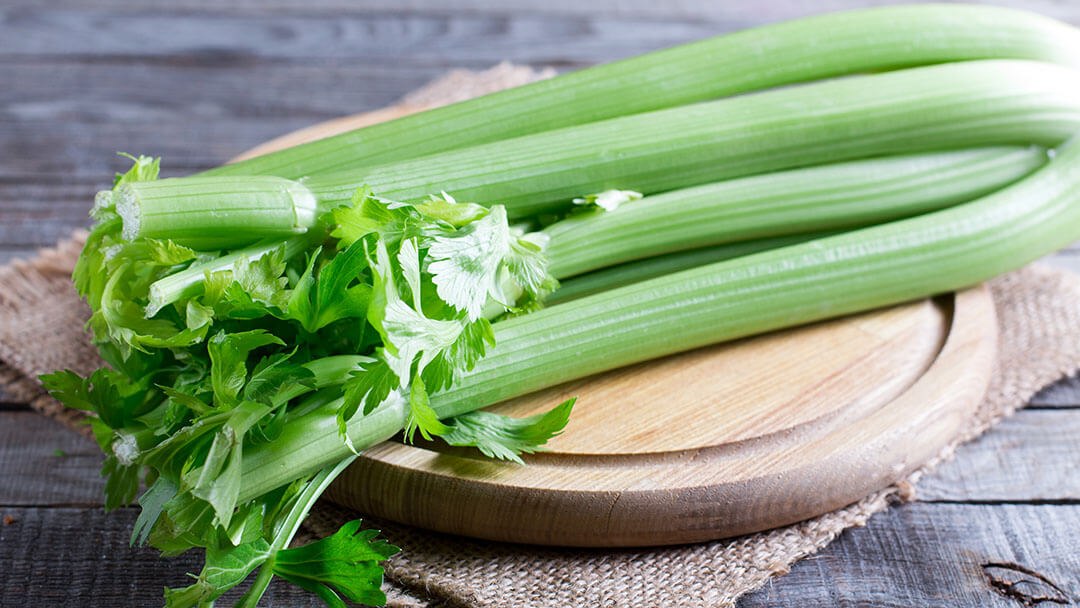 Fresh green celery stems on wooden cutting board