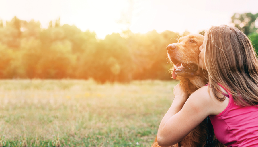 Woman sat with her dog outside in a field kissing it's face
