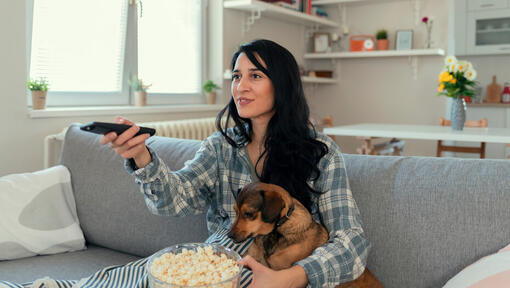 Woman watching tv with a bowl of popcorn and her dog