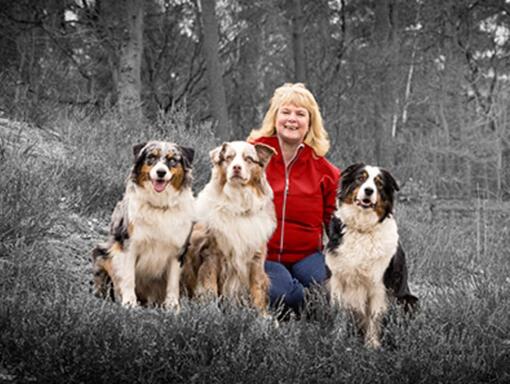 A woman with three dogs sits against the background of the forest