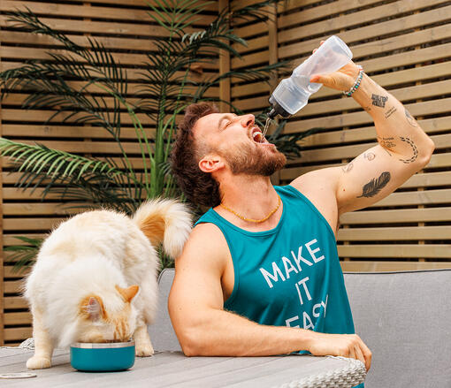 Sam Thompson sat outside drinking water with his cat drinking Hydralife